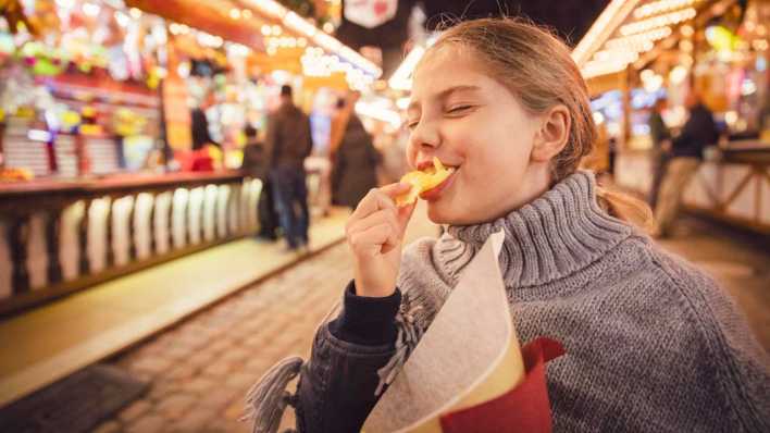 ARCHIV, München, 17.03.2020: Mädchen isst Chips auf einem Rummel (Bild: picture alliance / Westend61)