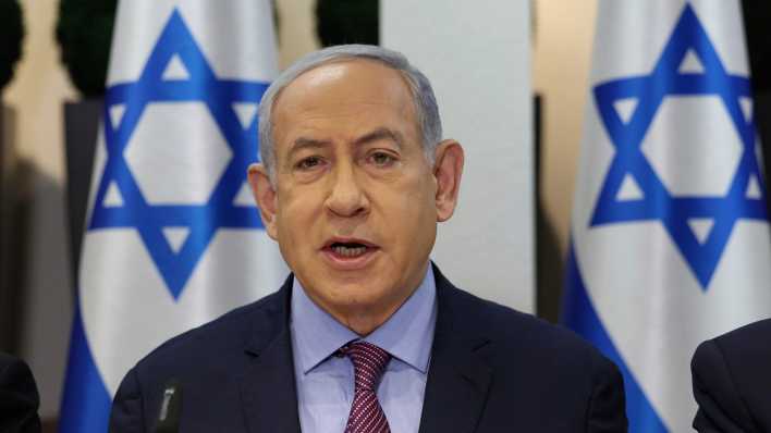 Benjamin Netanjahu bei einer Kabinettssitzung vor israelischen Flaggen.