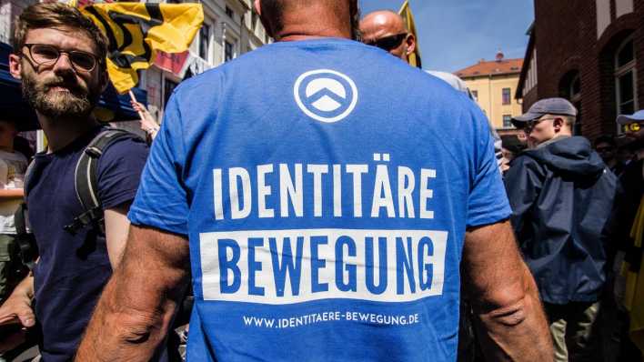 Ein Mann mit einem blauen Shirt, auf dem "Identitäre Bewegung" steht, steht auf einer Demonstration in Sachsen-Anhalt. (Bild: picture alliance / ZUMAPRESS / Sachelle Babbar)