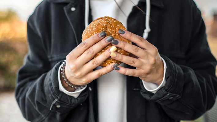 Hände mit Nagellack halten einen Burger (Bild. picture alliance / Westend61 / Aitor Carrera Porté)