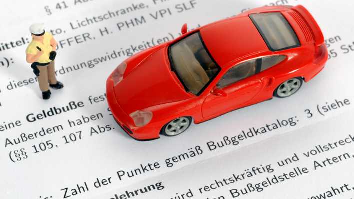 Eine Polizei-Figur steht neben einem Spielzeugauto. Darunter liegt ein Bußgeldbescheid mit Punkten.(Bild: picture-alliance / Eibner-Pressefoto )