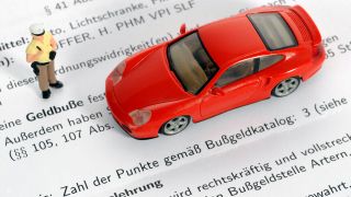 Eine Polizei-Figur steht neben einem Spielzeugauto. Darunter liegt ein Bußgeldbescheid mit Punkten.(Bild: picture-alliance / Eibner-Pressefoto )