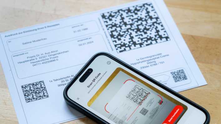 Ein Ausdruck eines E-Rezepts und die dazugehörige App auf einem Smartphone