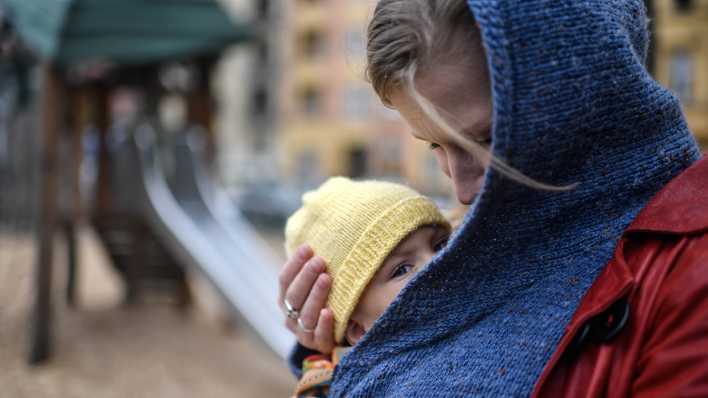 Mutter mit Kind im Tragetuch auf einem Spielplatz in Berlin-Neukölln