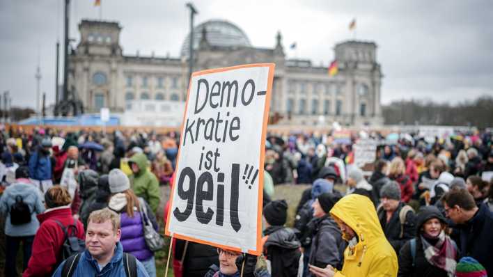 Eine Frau hält bei einer Demonstration vor dem Bundestag ein Plakat mit der Aufschrift "Demokratie ist geil" hoch.