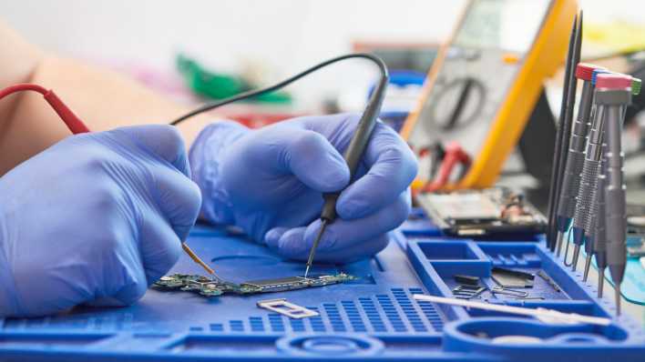 Mit einem Messgerät wird ein defektes Smartphone bei der Reparatur untersucht.