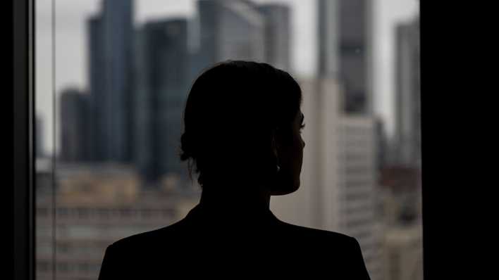 Eine Frau schaut aus einem Bürofenster auf weitere Hochhäuser (Bild: picture alliance/dpa/Hannes P. Albert)