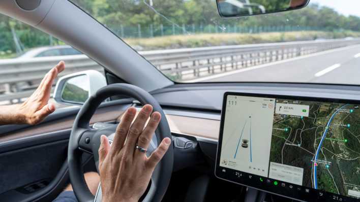 Mann fährt mit dem Tesla Model Y Auto auf der Autobahn mit Autopilot ohne Hände am Lenkrad