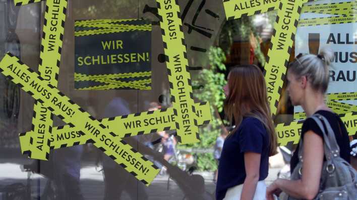 Aufkleber mit dem Hinweis "Wir schließen - alles muss raus" kleben auf dem Schaufenster eines Modegeschäfts in einer Fußgängerzone (Bild: IMAGO / Ralph Peters)