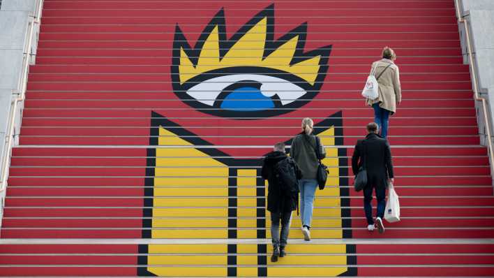 Teilnehmer der Leipziger Buchmesse gehen über eine Treppe mit dem Logo.