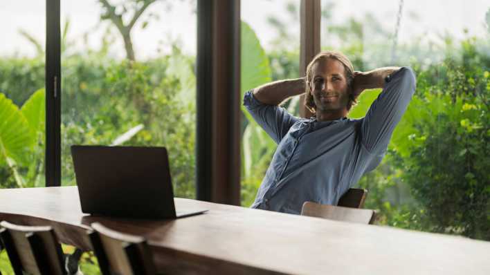 Ein Mann sitzt zufrieden an einem Laptop im Homeoffice (Bild: picture alliance / Westend61 | Steve Brookland)