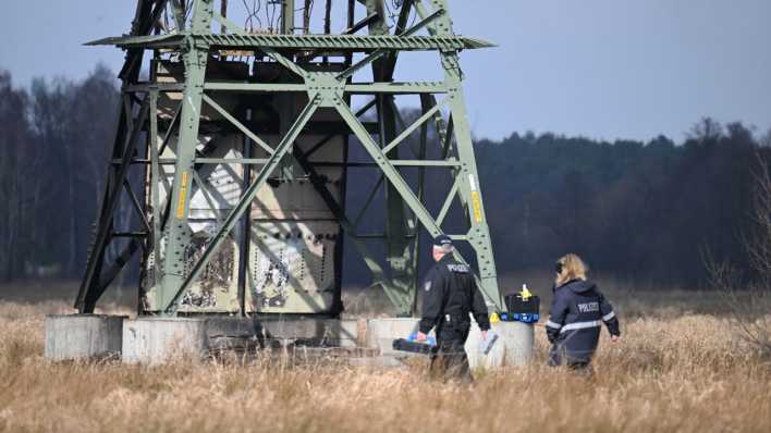 Die Polizei ermittelt an einem beschädigten Strommasten auf einem Feld in der Nähe der Tesla-Autofabrik in Grünheide (Bild: picture alliance/dpa/Sebastian Gollnow)