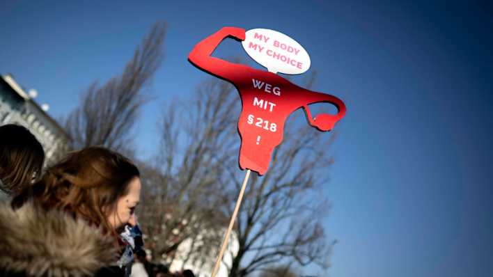 Eine Demonstrantin hält während des Internationalen Frauentags ein Schild mit der Aufschrift "Weg mit Paragraph 218" hoch (Bild: IMAGO / IPON)