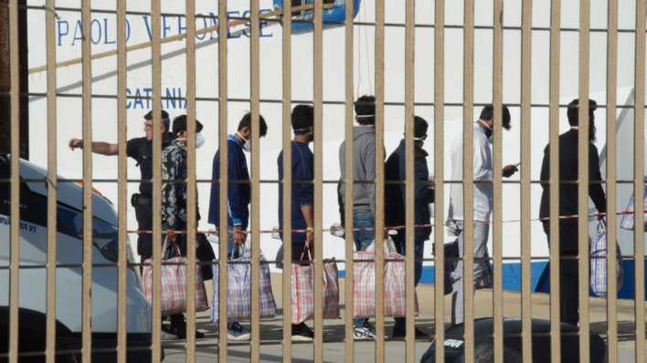 Asylsuchende stehen hinter einem Zaun in einem italienischen Hafen (Bild: picture alliance/ROPI/Resqship)