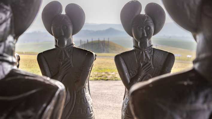 Repliken der Statue des "Keltenfürsten vom Glauberg" - mit Blick auf den großen Grabhügel - stehen beim Museumsgebäude der Keltenwelt am Glauberg.