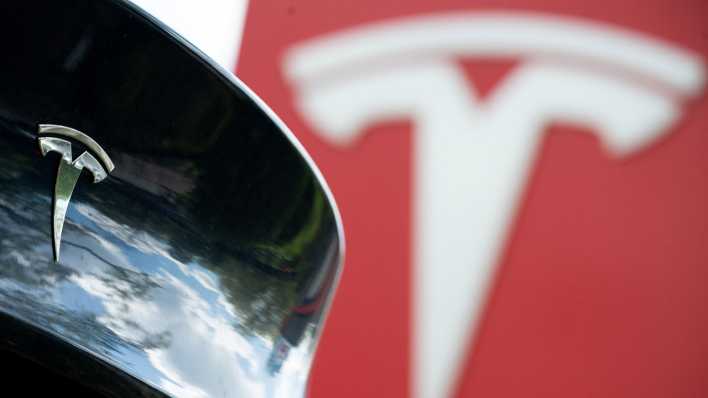 Das Tesla-Logo ist hinter einem Auto der Marke zu sehen (Bild: picture alliance/dpa/Sebastian Gollnow)