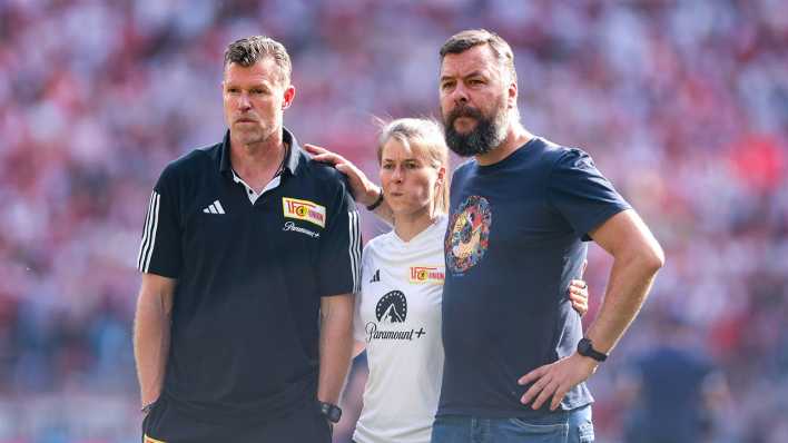Union Berlins Trainer Marco Grote, Co-Trainerin Marie-Louise Eta und Geschäftsführer Kommunikation Christian Arbeit stehen Arm in Arm am Spielfeldrand bei der Partie in Köln. (Archivbild)