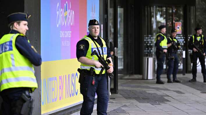 Polizisten stehen vor der Malmö-Arena, an der das Logo vom ESC zu sehen ist.