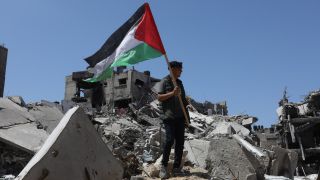 Ein Palästinenser hält die palästinensische Fahne in der Hand, während er auf Trümmern nach israelischem Beschuss stehtt.