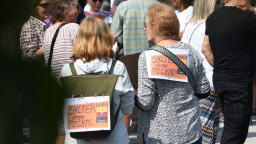 "Sylterinnen gegen Rechts!“ steht auf Plakaten, die zwei Frauen bei einer Mahnwache auf Sylt auf ihre Rücken geheftet haben.
