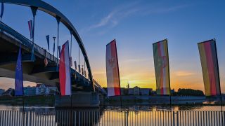 Fahnen wehen im Wind zum Sonnenaufgang vor der Stadtbrücke über den Grenzfluss Oder zwischen Frankfurt (Oder) und dem polnischen Slubice.