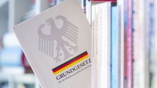 Ein Grundgesetz steckt in einem Bücherregal (Bild: picture alliance/dpa/Hendrik Schmidt)