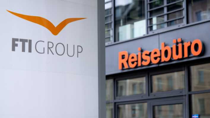 Das Logo des Reiseveranstalter FTI (FTI Group) steht an der Firmenzentrale vor einem Reisebüro.