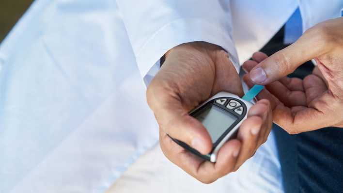 Ein Arzt führt einen Teststreifen in das Blutzuckermessgerät zur Diabetes-Diagnostik.