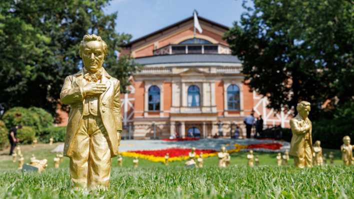 Goldfarbene Wagner-Figuren des Konzeptkünstler Ottmar Hörl stehen im Rahmen der Kunstinstallation "Verneigung" vor dem Festspielhaus vor Beginn der Bayreuther Festspiele.
