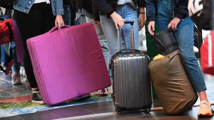 Jugendliche warten mit Koffer, Isomatten, Schlafsack und Matratze.