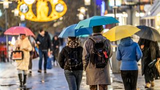 Passanten gehen mit Regenschirmen über eine Einkaufsstraße in Essen.