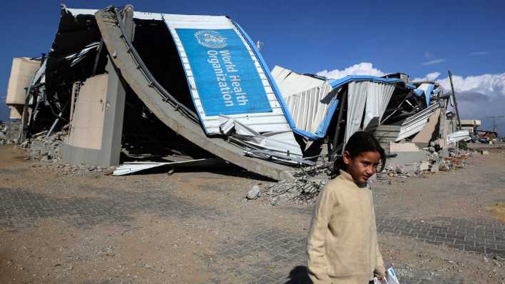 Zerstörtes WHO-Gebäude und Flüchtlingskind im Gazastreifen (Bild: IMAGO/NurPhoto/Majdi Fathi)
