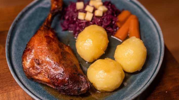 Gänsekeule mit Kartoffelknödeln, Rotkraut, Möhren und Apfelstückchen liegt an Heiligabend angerichtet auf einem Teller.