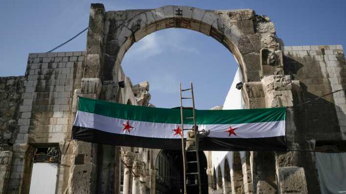 Ein Arbeiter hängt eine Flagge der syrischen Revolutionäre - grün, weiß, schwarz mit roten Sternen am Eingang zu dem Suq al-Hamidiya, vor dem Freitagsgebet auf.