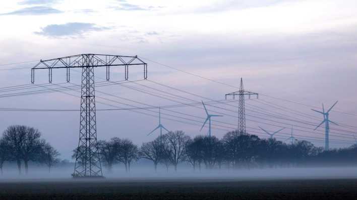 Stromleitungen und Strommasten im Nebel an einem Feld in Nauen.