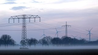 Stromleitungen und Strommasten im Nebel an einem Feld in Nauen.