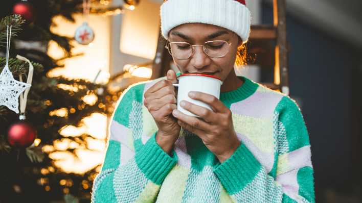 Junge Frau riecht zu Weihnachten an einem Getränk