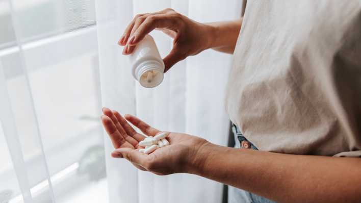Frau schüttet sich Tabletten auf die Hand