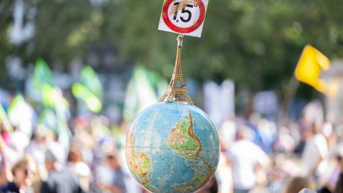 Einen Globus mit einem Miniatur-Eiffelturm und dem 1,5-Grad Ziel des Pariser Klimaschutzabkommens trägt ein Mann auf einer Demonstration.