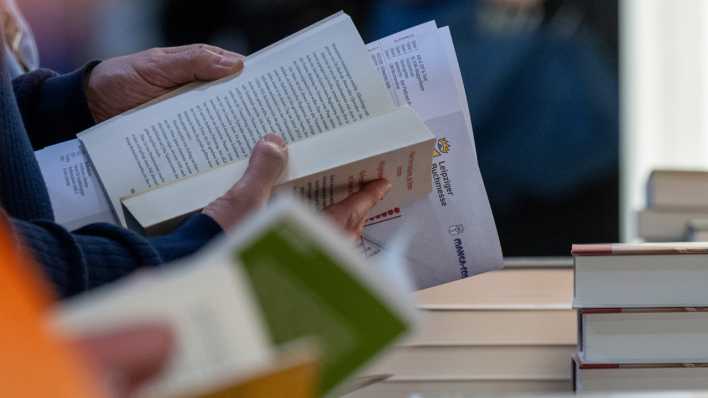 Besucher der Leipziger Buchmesse lesen an einem Stand.
