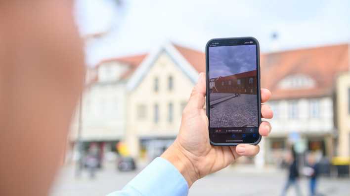 Teilnehmer einer Presseveranstaltung probiert mit einem Mobiltelefon ein Programm aus, das mit Hilfe von Augmented-Reality die Mauer eines "Domus Mercatorum" an der Stelle zeigt, an der sie einst stand (Bild: picture alliance/dpa/Klaus-Dietmar Gabbert) Teilnehmer einer Presseveranstaltung probiert mit einem Mobiltelefon ein Programm aus, das mit Hilfe von Augmented-Reality die Mauer eines "Domus Mercatorum" an der Stelle zeigt, an der sie einst stand (Bild: picture alliance/dpa/Klaus-Dietmar Gabbert)