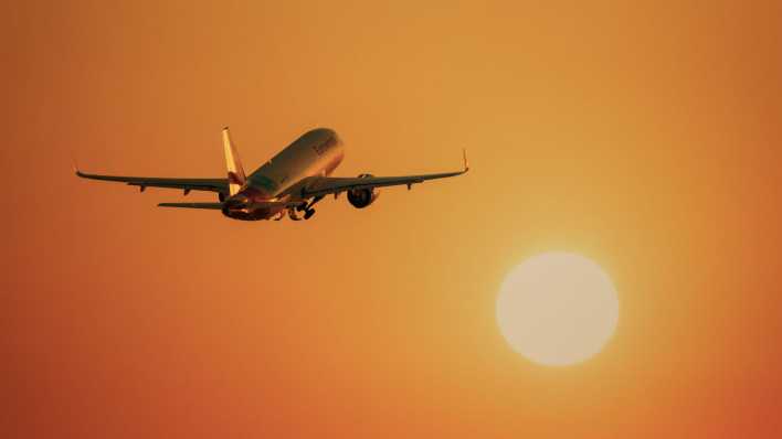 Flugzeug fliegt in Richtung einer großen, orange leuchtenden Sonne (Bild: picture alliance/imageBROKER/Lilly)