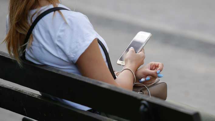 Eine junge Frau hält ein Smartphone in der Hand.