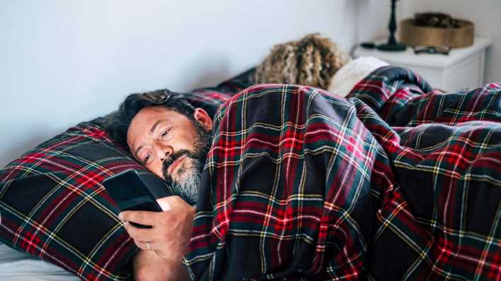 Mann mit Smartphone liegt im Bett