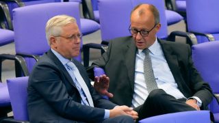 Norbert Röttgen und Friedrich Merz unterhalten sich auf Stühlen im Bundestag.