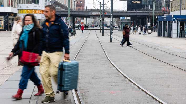 Reisende gehen während des BVG-Warnstreiks über die leeren Tramgleise am Alexanderplatz.