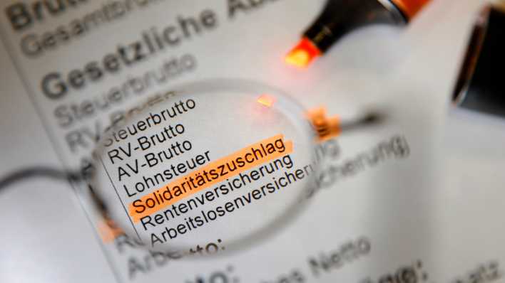 Durch eine Brille ist der Posten "Solidaritätszuschlag" auf einem Gehaltsschein zu sehen