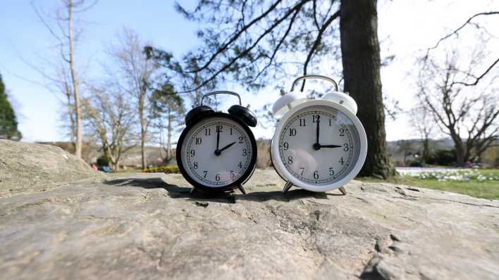 Ein Wecker zeigt zwei Uhr und der andere drei Uhr. Die Uhren werden am Sonntag den 30.03.2025 auf Sommerzeit umgestellt.