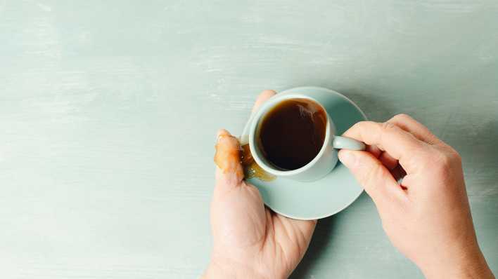 Zitternde Hände verschütten Kaffee aus einer Tasse.
