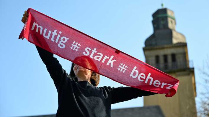 Eine junge Frau hält einen Kirchentagsschal mit der Losung "mutig - stark - beherzt".